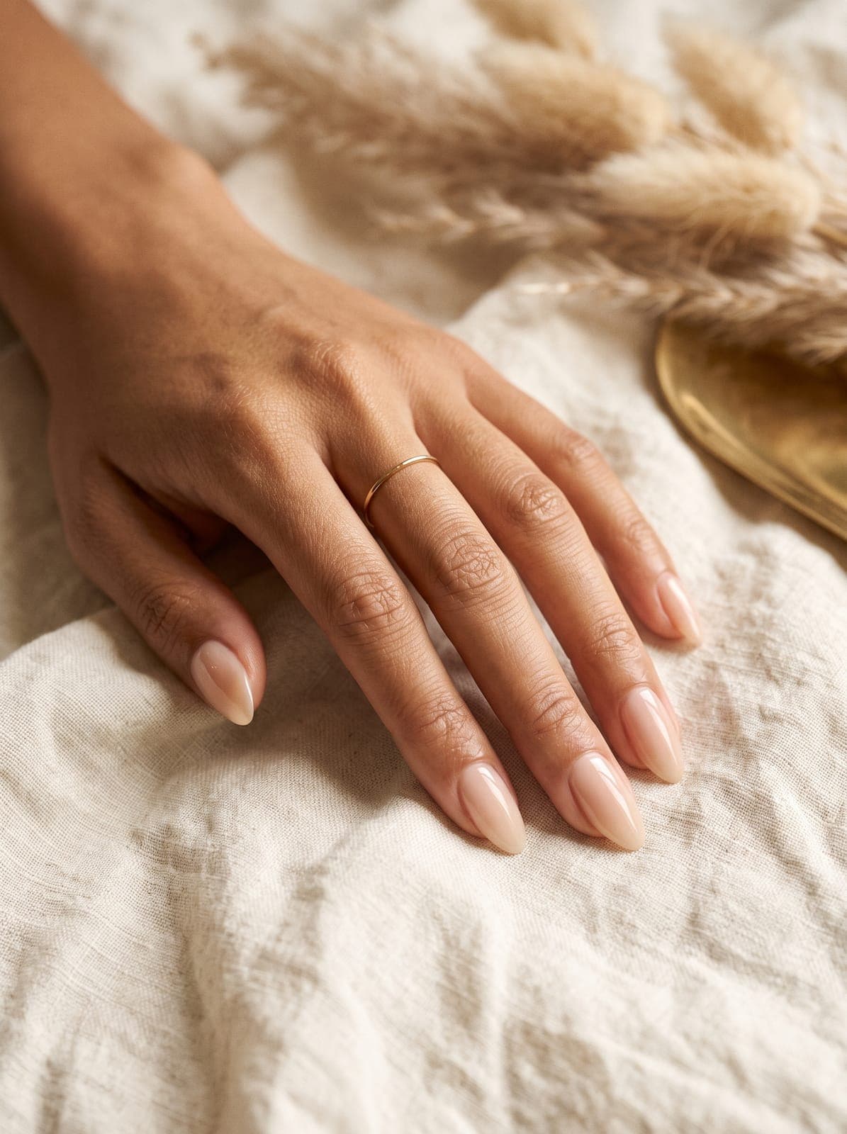 Manucure milky nude sur ongles amande, main posée sur du lin crème